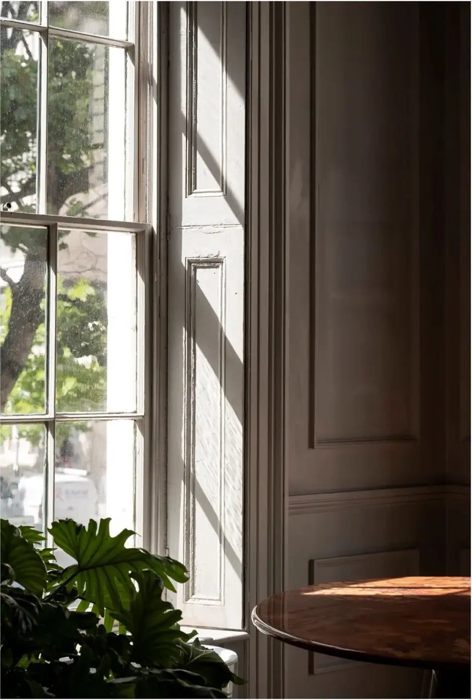Sitting area beside tall sash windows with dado panelling and a round wooden table